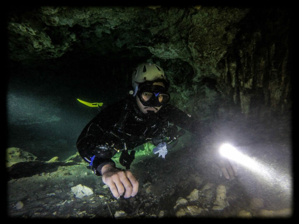 Cave diver navigates a cave system wearing a dive torch and helmet Cave diver navigates a cave system wearing a dive torch and helmet