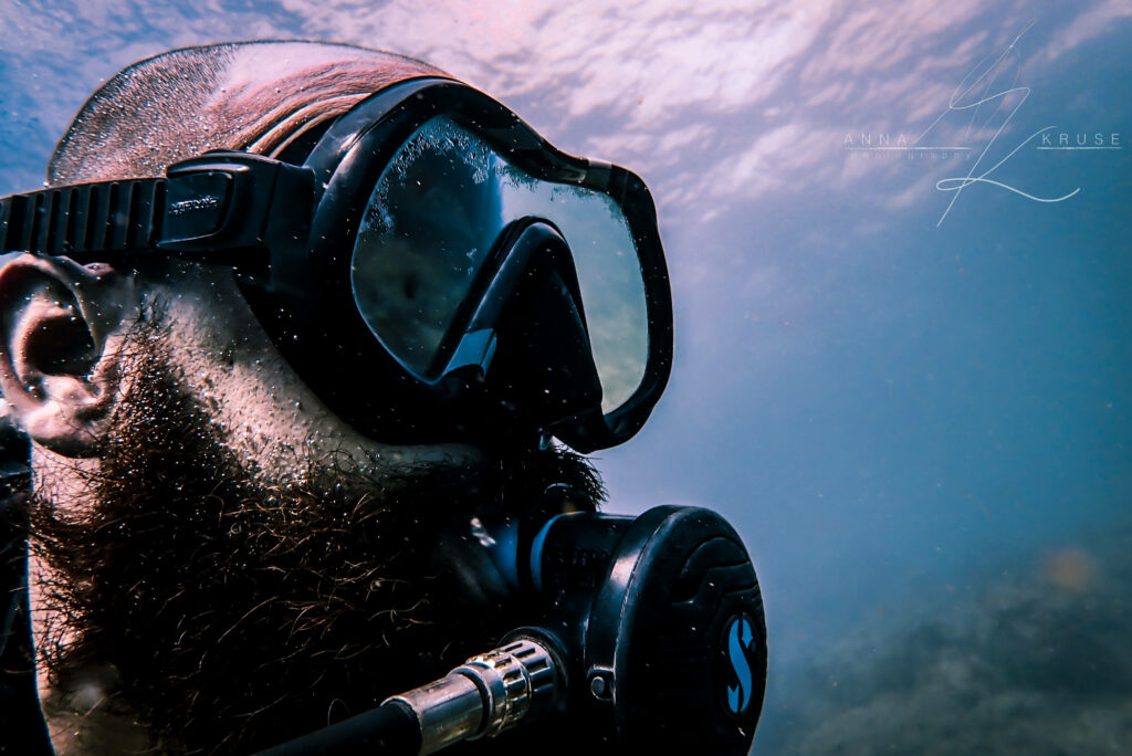 Photo Credit: Anna Kruse (IG: AnnaUnderTheSea) Bearded diver with a Scuba Pro regulator and reflective mask