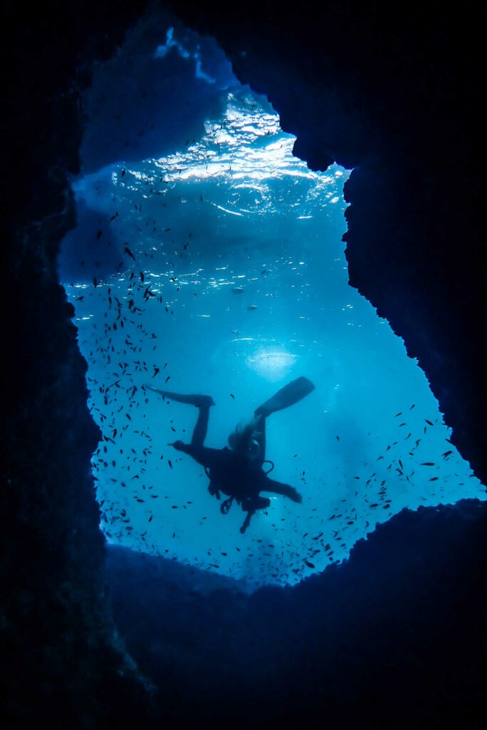 Photo Credit: Anna Kruse (IG: AnnaUnderTheSea) A scuba diver exiting a swim-through at Malong dive site