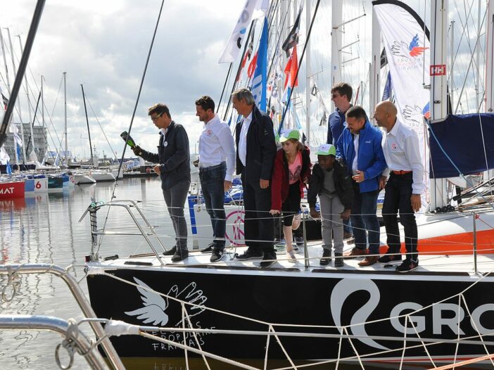 A group of people gather at a boat christening ceremony as the owner prepares to break a bottle of champagne over the bow of the boat