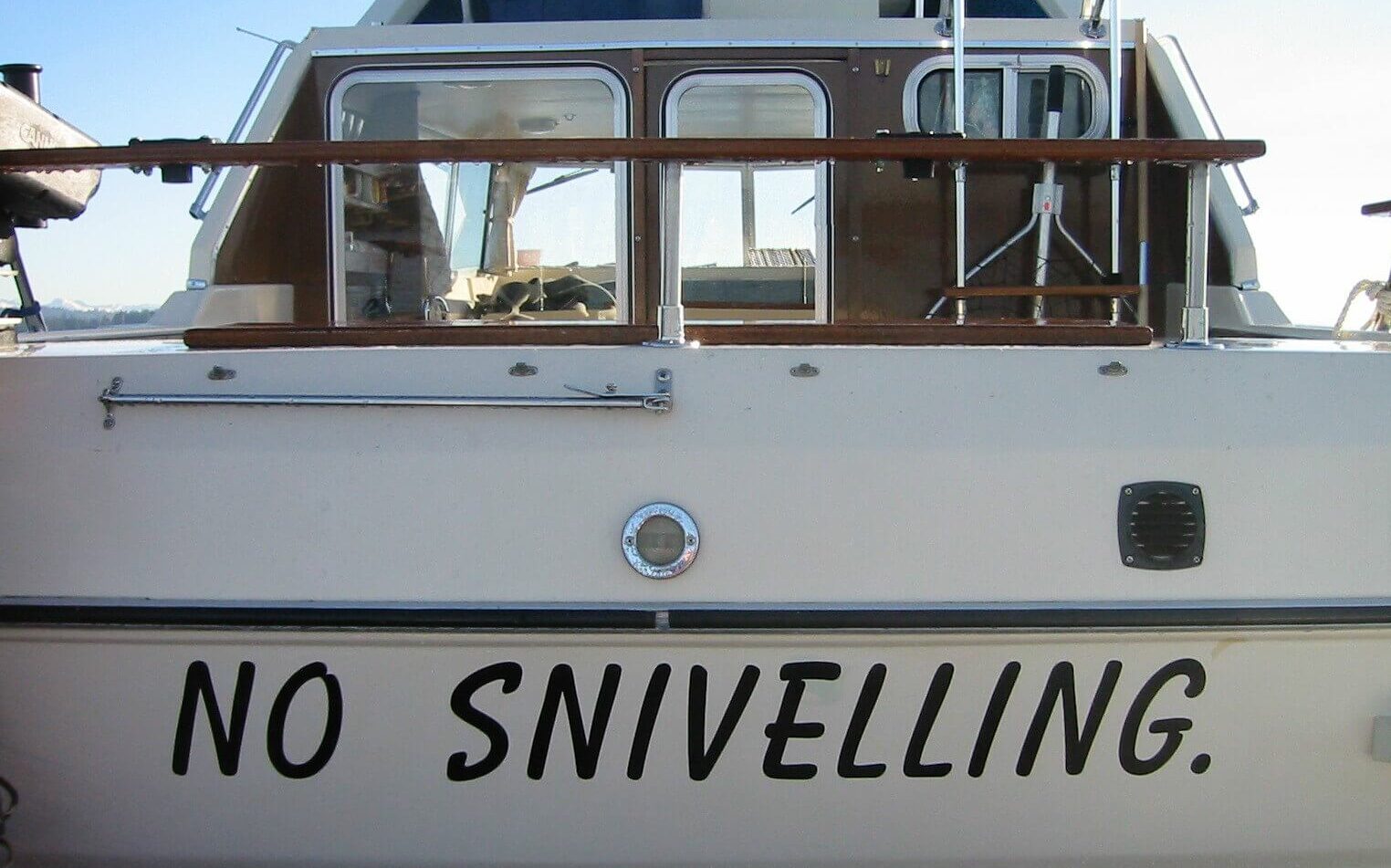the name "No Sniveling" painted at the bow of a white sailboat with dark brown woodwork the name "No Sniveling" painted at the bow of a white sailboat with dark brown woodwork