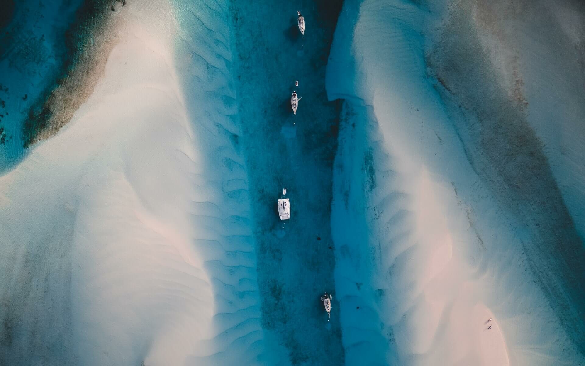 Aerial view of sailboats in the Bahamas Four sailboats anchored in shallow blue Caribbean water between two sandbars