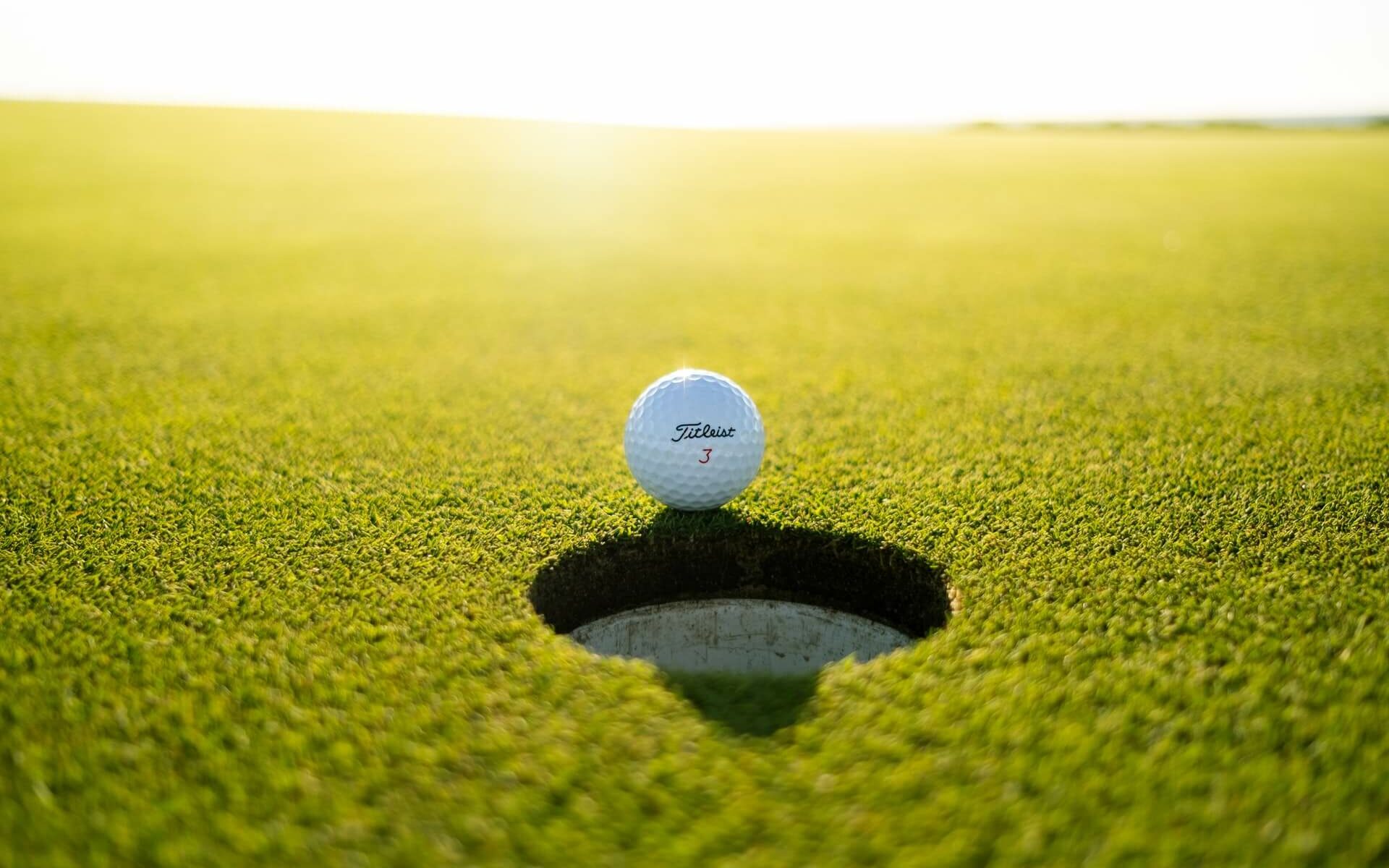 Golfing in the Bahamas A Titleist 3 golf ball sitting at the very edge of the hole on a putting green in the Bahamas