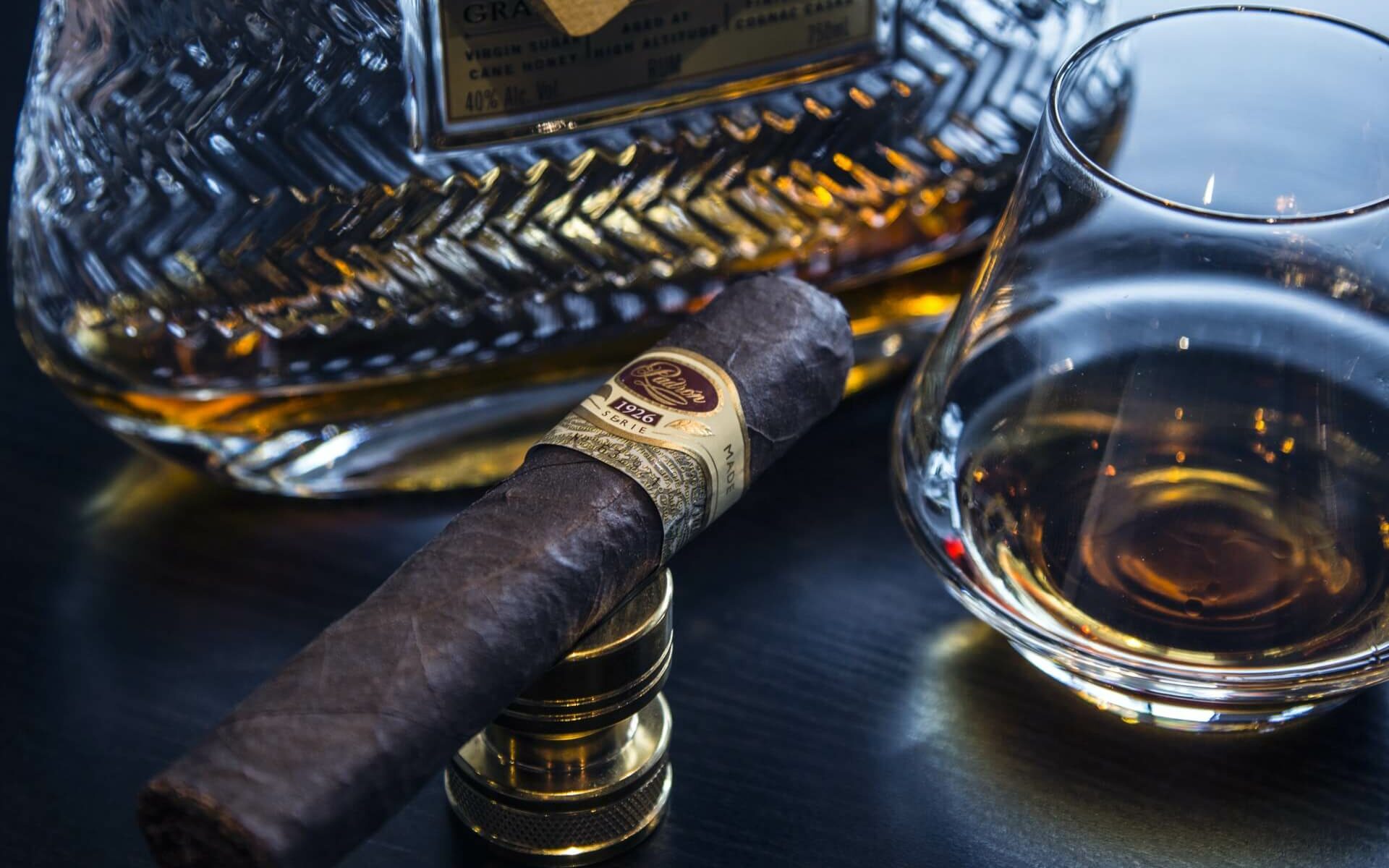 Cigars and Rum in the Bahamas A hand rolled Bahamian cigar sits next to a glass of rum on a dark wooden table