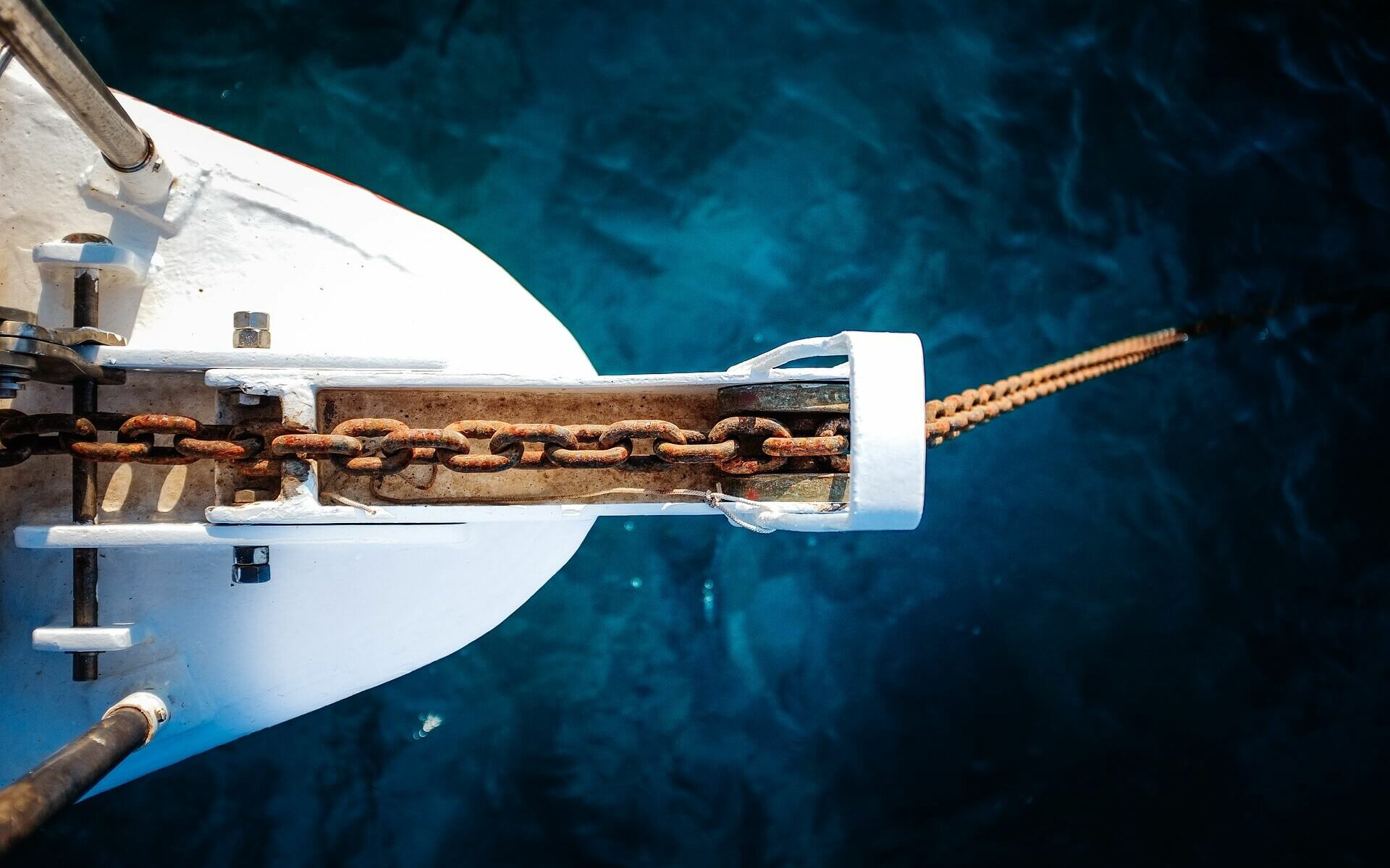 an anchor chain hangs off the bow of a white boat into cobalt blue waters an anchor chain hangs off the bow of a white boat into cobalt blue waters