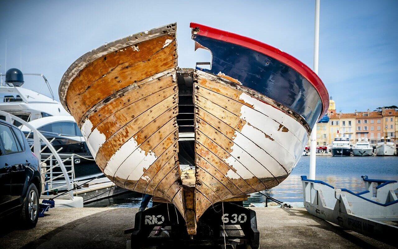 A boat sits on a trailer with deterioration showing on the exterior of the hull, showing how the cost of boat ownership includes boat depreciation A boat sits on a trailer with deterioration showing on the exterior of the hull, showing how the cost of boat ownership includes boat depreciation