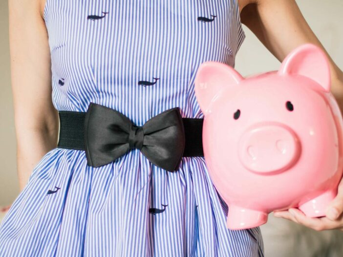 Woman in a blue whale dress holds a pink piggy bank