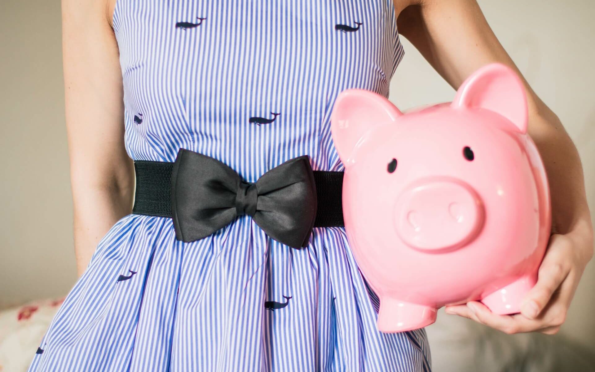 Woman in a blue whale dress holds a pink piggy bank to signify the cost of boat ownership Woman in a blue whale dress holds a pink piggy bank to signify the cost of boat ownership