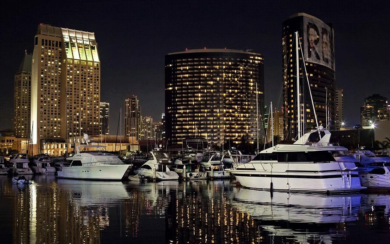 Several boats are parked at a marina at night in front of a city skyline Several boats are parked at a marina at night in front of a city skyline